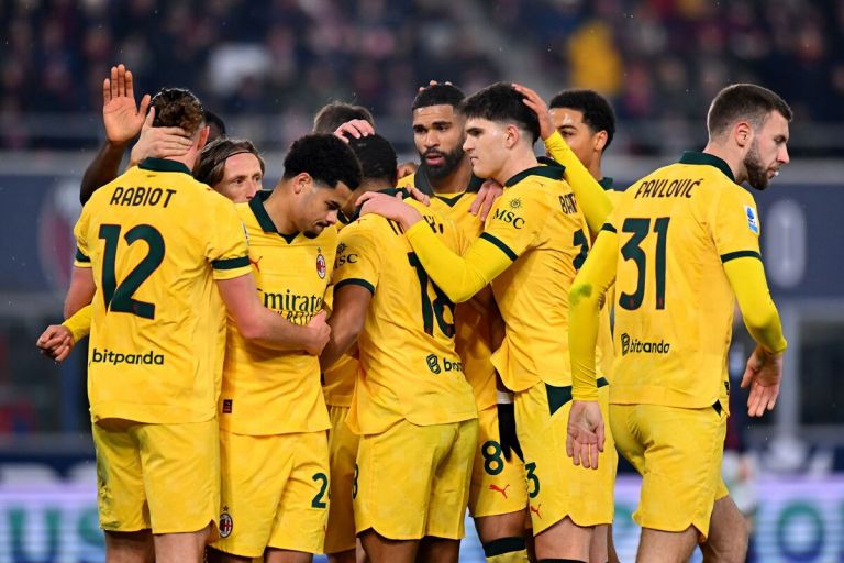 Adrien Rabiot, Strahinja Pavlovic, and AC Milan teammates huddle together to celebrate a goal against Bologna in their yellow away kit.