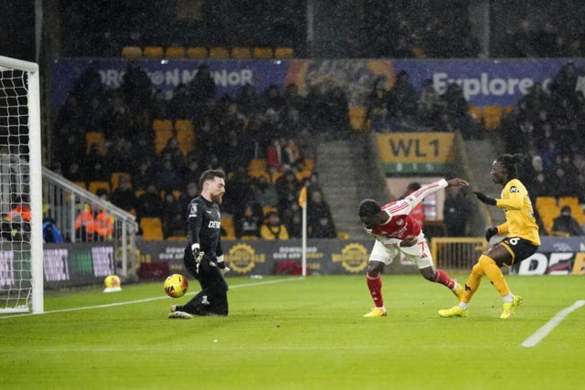A Wolves forward strikes the ball past the Arsenal goalkeeper into the net while Arsenal defenders watch in shock.